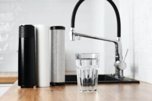 A glass of clean fresh water and set of filter cartridges on wooden table in a kitchen interior.