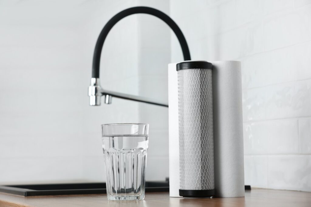 A glass of clean fresh water and set of filter cartridges on wooden table in a kitchen interior.