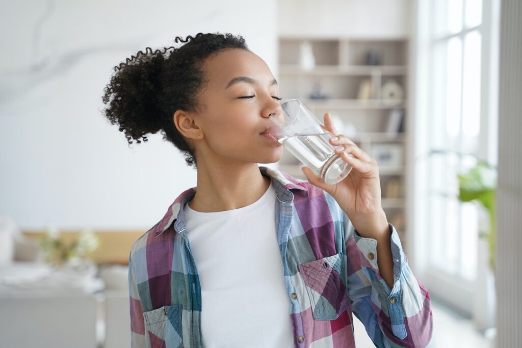 African american young girl enjoy drinking pure filtered water from glass at home. Healthy lifestyle