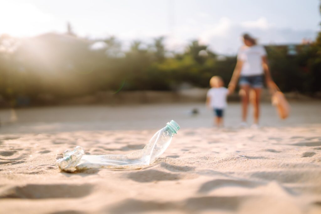 Child with mother collects plastic, garbage on the beach by sea. Empty used dirty plastic bottles.