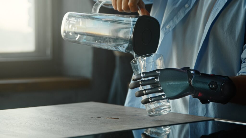 Disabled guy with bio hand prothesis pours water into glass from bowl and drinks standing in kitchen