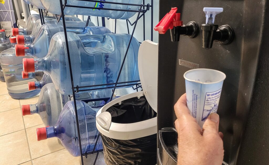 Drinking cup of water after a workout in hot and cold dispenser in workout area.