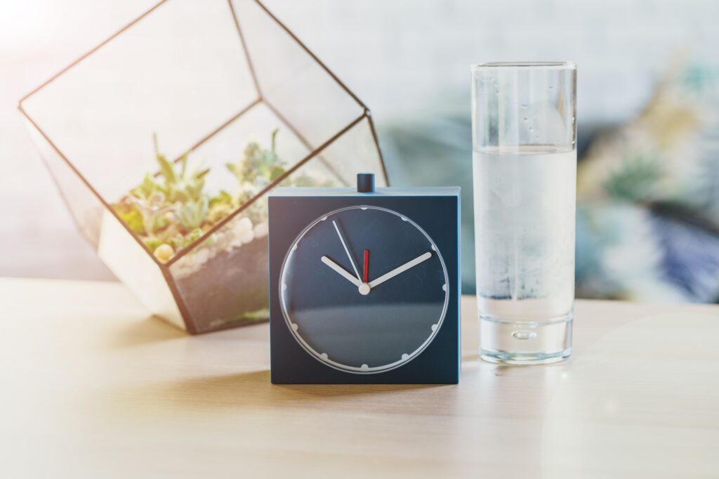 Drinking water health concept. Alarm clock and glass of water on table