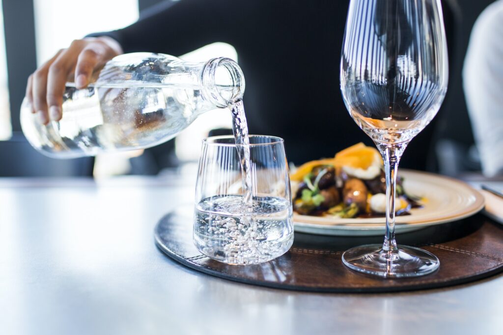 Midsection of woman pouring water into glass at restaurant