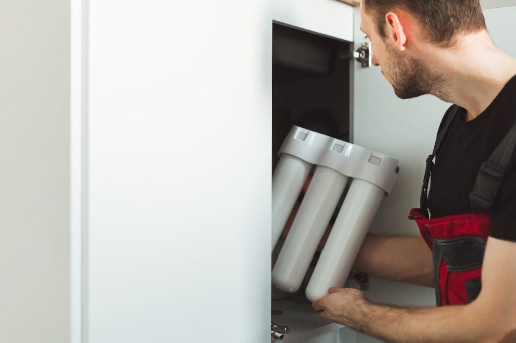 Plumber in the kitchen installs a household water treatment system. Three stage flask system