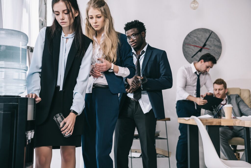 tired businesspeople standing in queue for water dispenser at office