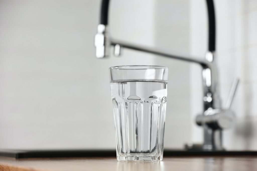 Transparent glass of clean filtering water on wooden table in kitchen interior. Tap with purified