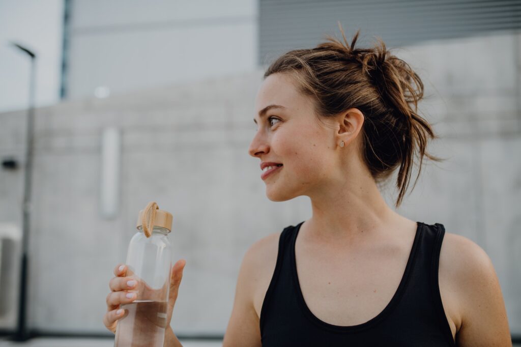 Young woman drinking water during jogging in city, healthy lifestyle and sport concept.